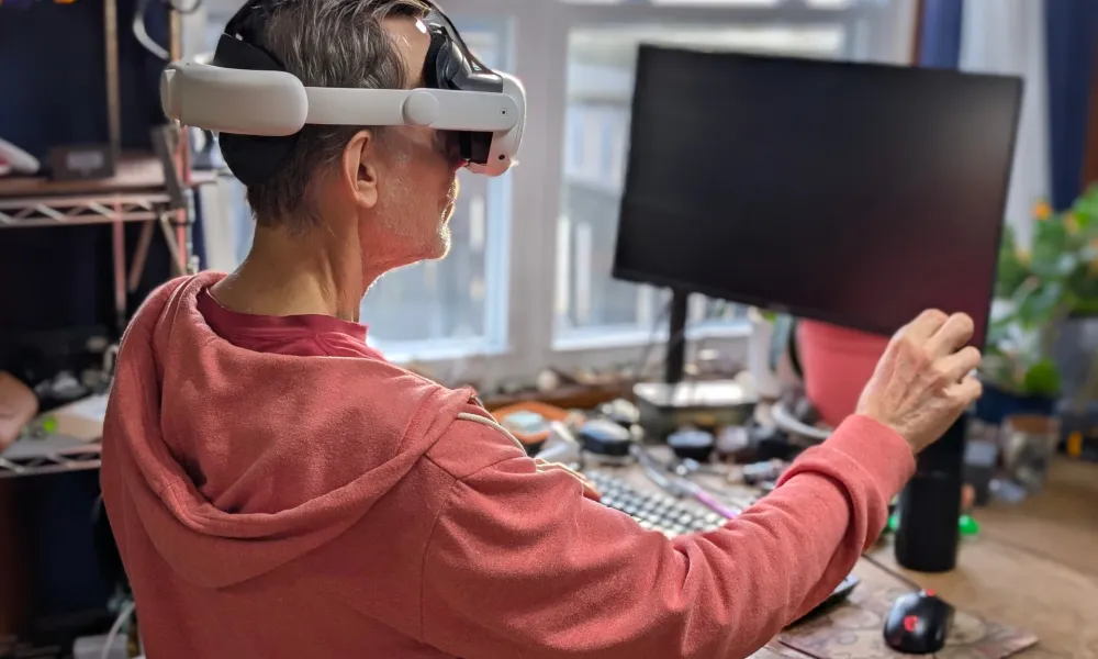 Alan-Truly-sits-in-front-of-a-Windows-PC-and-adjusts-a-virtual-screen-while-wearing-a-Meta-Quest-3-VR-headset